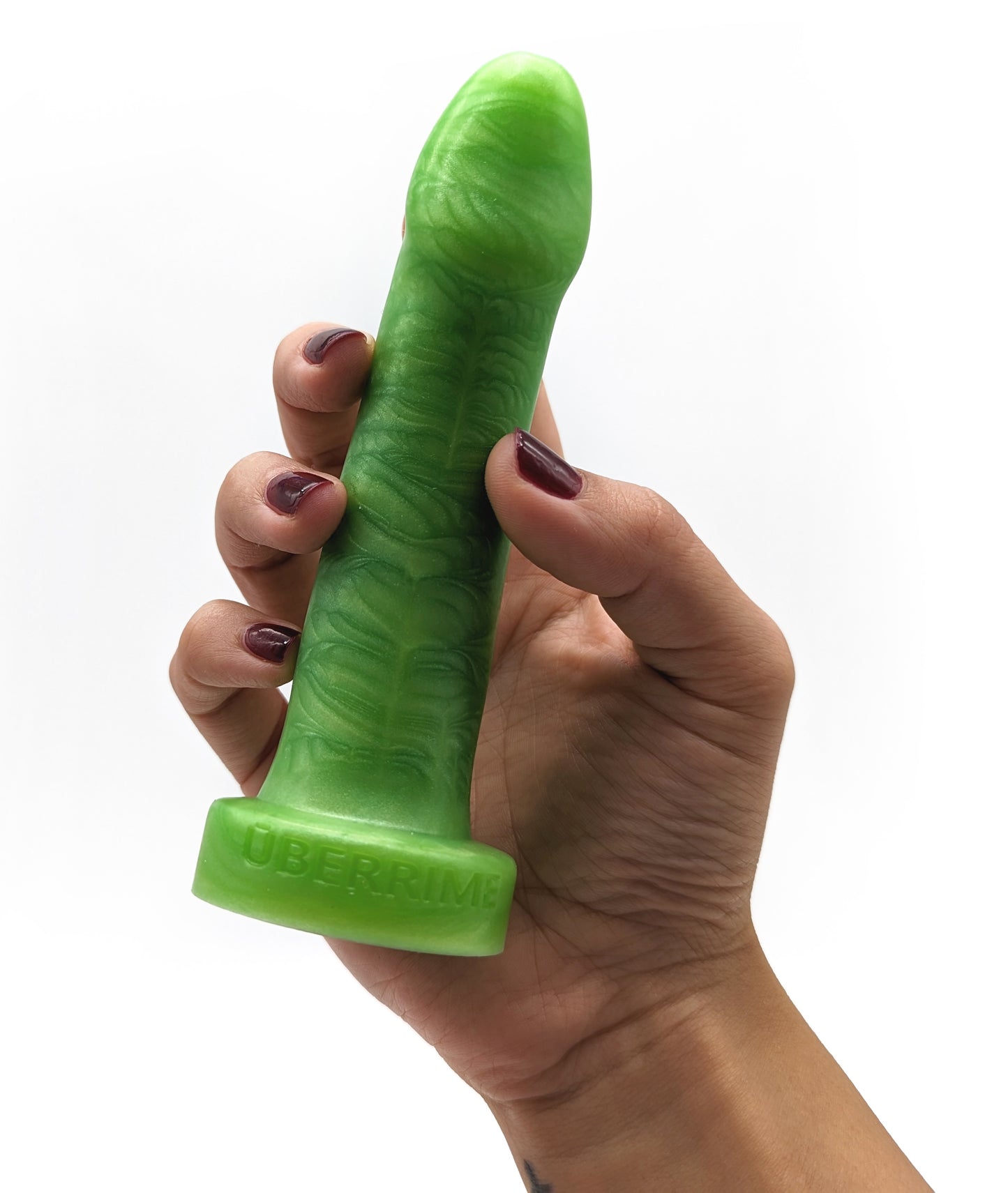 A hand holding up a beginner-friendly silicone dildo, the Uberrime Essential Model A. The toy is a semi-realistic design with an abstractly defined head and subtly curved shaft for g-spot stimulation. It has a flat, flared base. 
